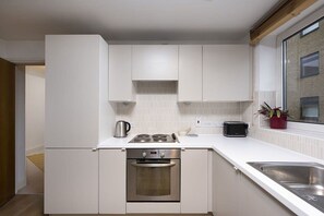 A modern kitchen with white cabinetry, a built-in oven, a stovetop, and a window with a view of the outside. - Charming 1 Bedroom Flat in Lambeth (London)