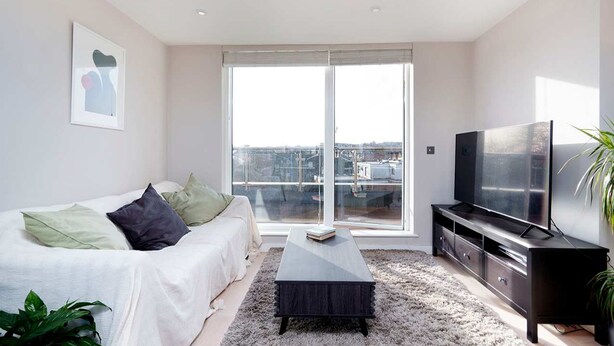 A modern living room with a sofa, a coffee table, a TV, and a large window offering a city view. - Charming 1-bedroom Flat in London (London)