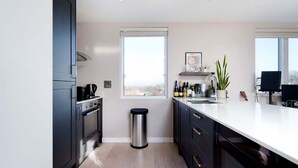 A modern kitchen with dark cabinets, a stainless steel trash can, a window with a view, and a countertop with various items. - Charming 1-bedroom Flat in London (London)