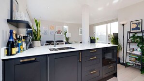 A modern kitchen with dark cabinetry, a white countertop, and a large window providing natural light. - Charming 1-bedroom Flat in London (London)