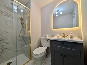 Ett modernt badrum med en duschavdelning med glasväggar, en vit toalett och en tvättställsmöbel med spegel.