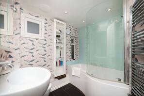 Een badkamer met een witte wastafel, een douche met glazen wanden en een wastafelmeubel met spiegel en planken.
