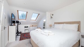 A modern bedroom with a large bed, two skylights, a desk, and a TV. - Charming 3-bedroom Flat in Prime Location (London)