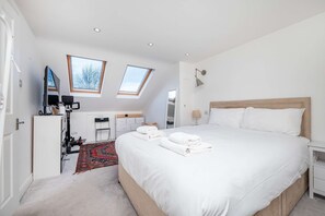 A modern bedroom with a large bed, two skylights, a desk, and a TV. - Charming 3-bedroom Flat in Prime Location (London)
