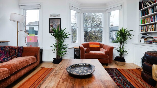 A cozy living room with a wooden coffee table, two sofas, a bookshelf, and large windows. - Charming 3-bedroom Flat in Prime Location (London)