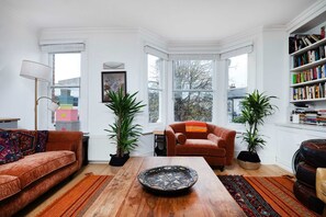 Een gezellige woonkamer met een houten salontafel, twee banken, een boekenkast en grote ramen.