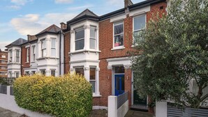 A row of terraced houses with white and red brick facades, bay windows, and a blue door. - Charming 3-bedroom Flat in Prime Location (London)