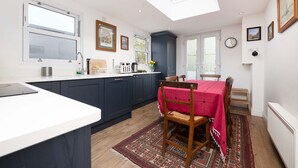 A modern kitchen with a skylight, dark blue cabinets, a white countertop, and a dining area with a red tablecloth. - Charming 3-bedroom Flat in Prime Location (London)