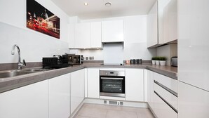 A modern kitchen with white cabinets, a stainless steel sink, and a built-in oven. - Stunning 2BR Flat With Balcony (Maidenhead)