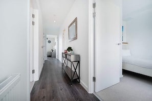 A hallway with a wooden floor, white walls, and a bed with white bedding in the room. - Stunning 2BR Flat With Balcony (Maidenhead)