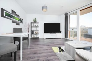 A modern living room with a flat-screen TV, a dining table, and a sofa. - Stunning 2BR Flat With Balcony (Maidenhead)