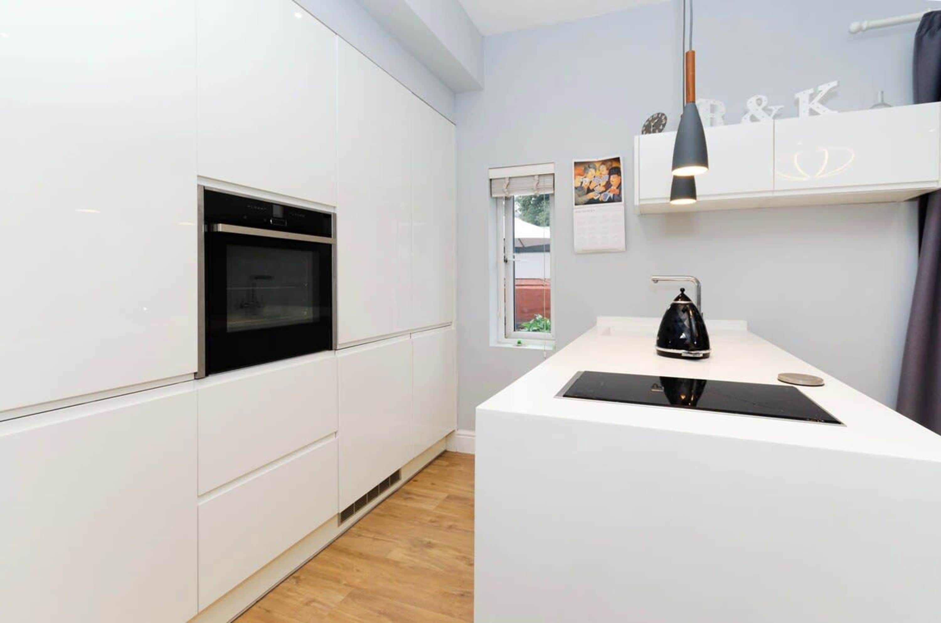A modern kitchen with white cabinetry, a built-in oven, a black countertop, and a pendant light.