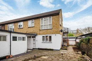 A two-story house with a white exterior, a tiled roof, and a small front yard with a stone pathway. - Charming Ground Floor Flat in Twickenham (Twickenham)