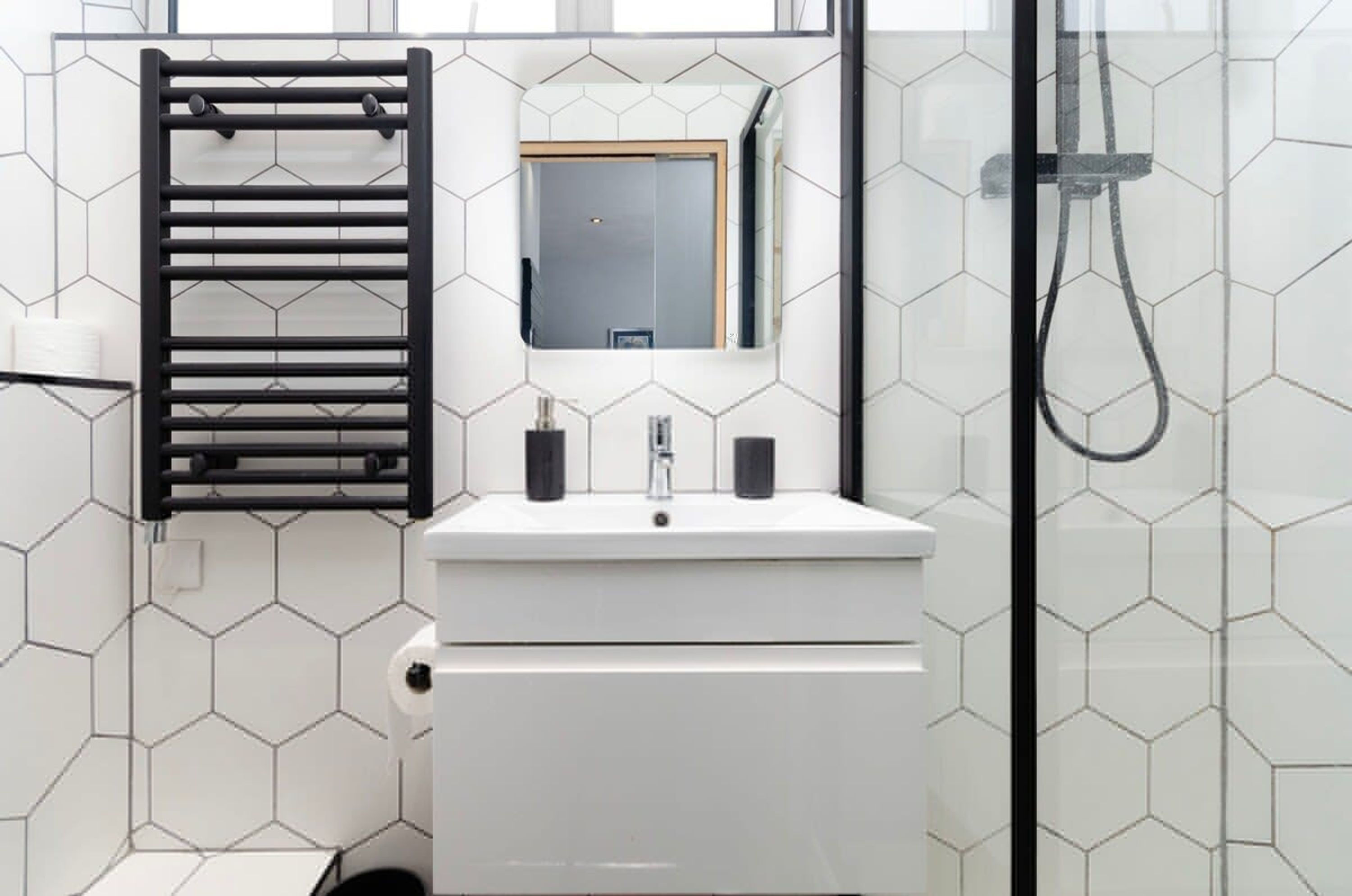 A modern bathroom with a white sink, black towel rack, and a glass-enclosed shower.