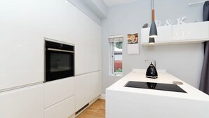 A modern kitchen with white cabinetry, a built-in oven, a black countertop, and a pendant light. - Charming Ground Floor Flat in Twickenham (Twickenham)