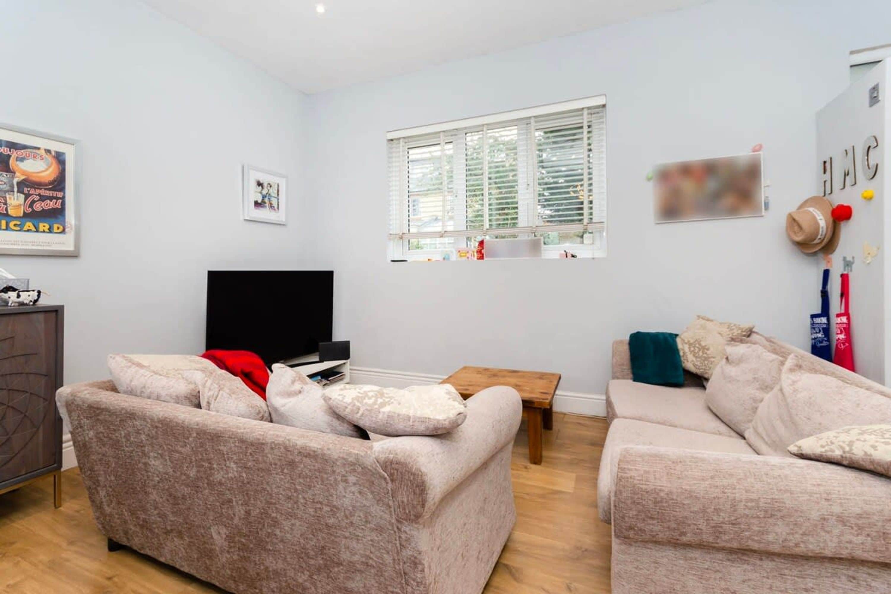 A living room with two beige sofas, a wooden coffee table, a flat-screen TV, and a window with blinds.