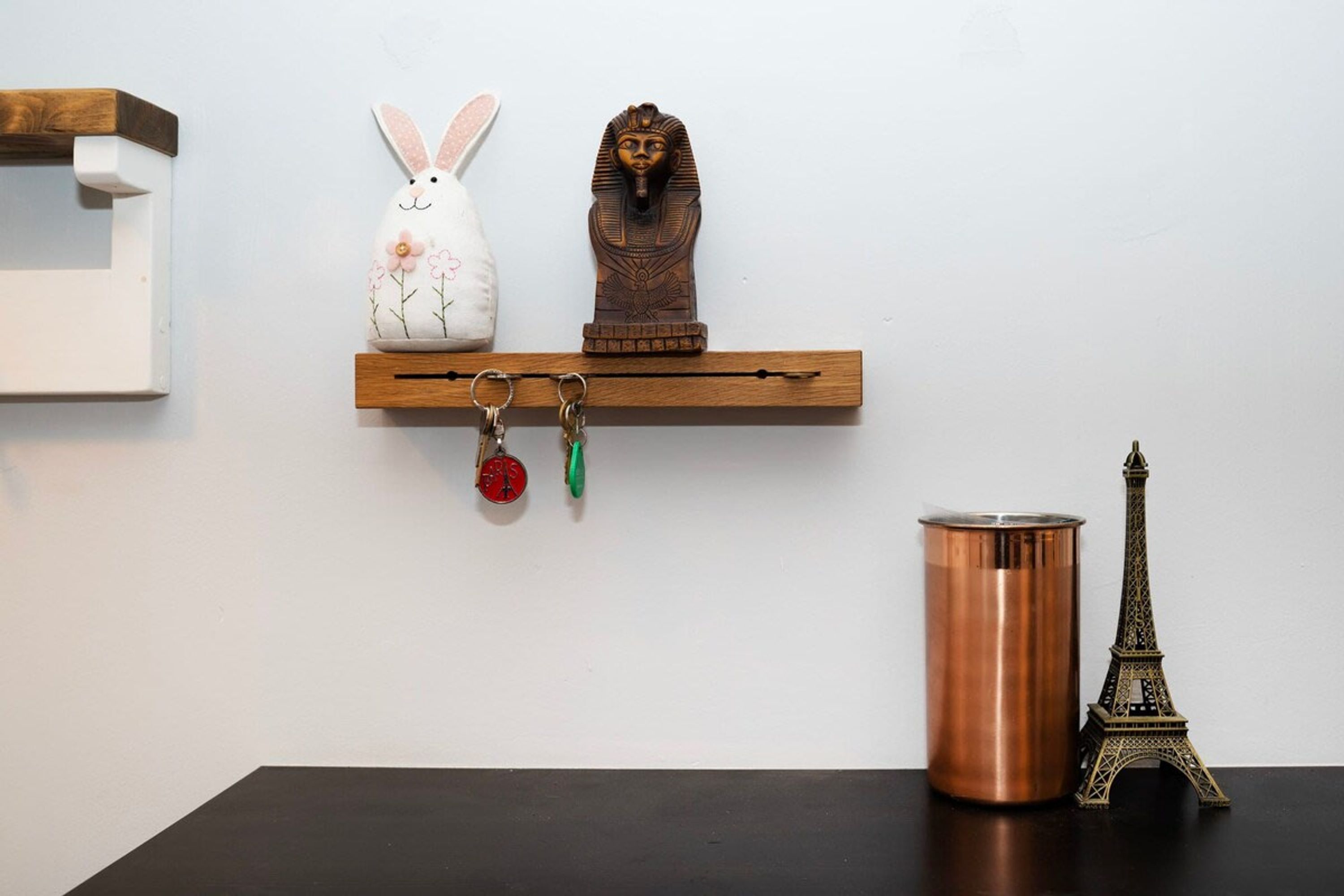 Une étagère avec une statuette de lapin blanc, un obélisque égyptien, une petite maquette de la Tour Eiffel, un pot en cuivre et un porte-clés orné d’un objet rouge et vert.