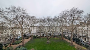 A view of a park with a lawn and trees, surrounded by rows of traditional buildings. - Stylish 1 Bed in SW7 With Private Balcony (London)