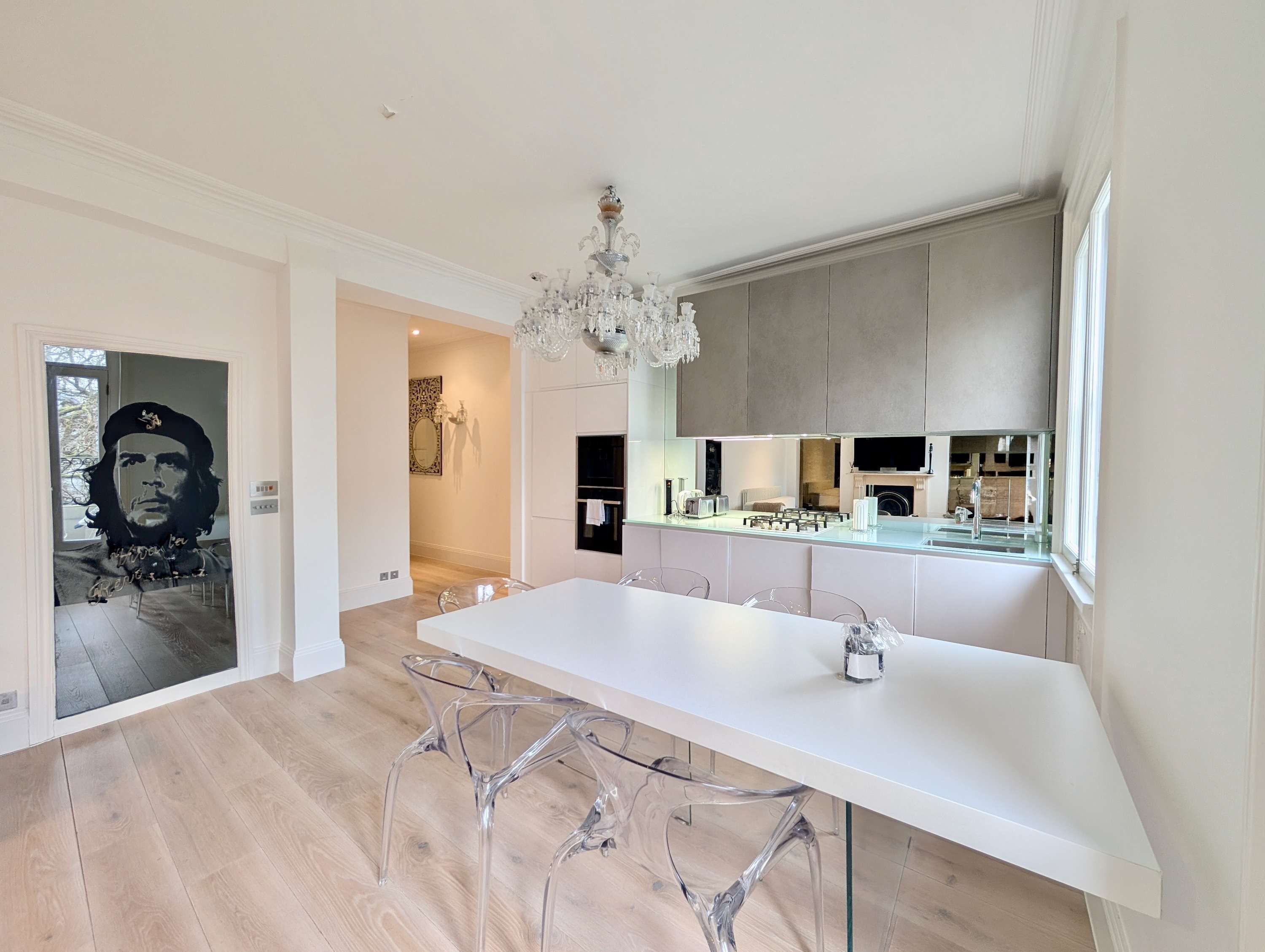 A modern kitchen with a large island, clear chairs, and a chandelier.