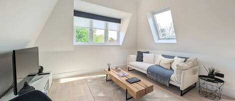 Un salon moderne avec un plafond haut, un canapé, une table basse, un téléviseur et une fenêtre.
