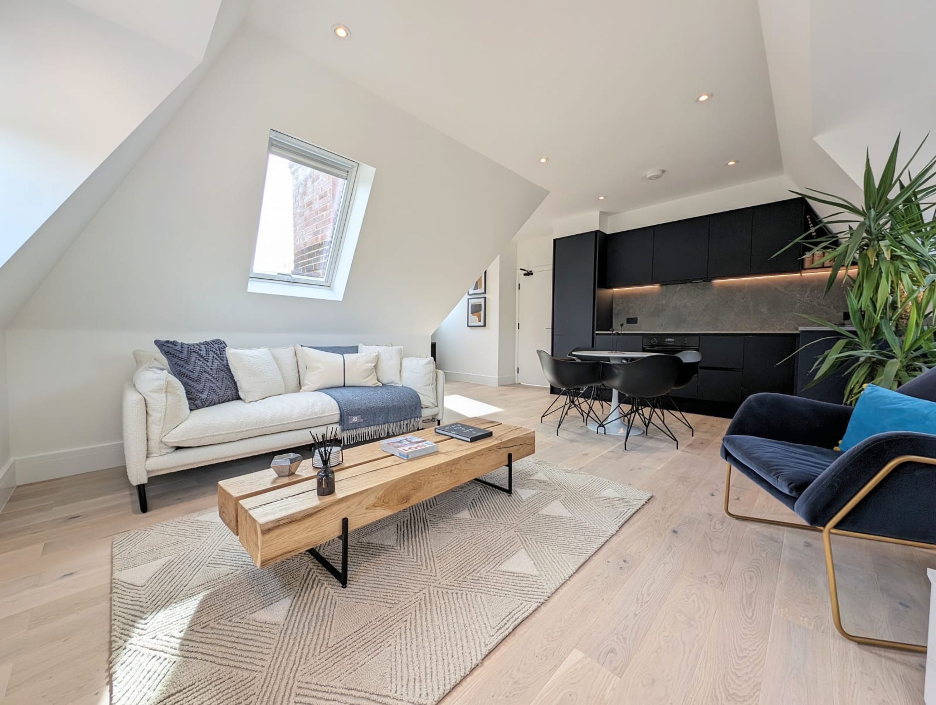 En moderne loftlejlighed med højt til loftet, et spiseområde med et sort bord og stole, en sofa med et geometrisk pyngetæppe, og et køkken med mørke skabe.