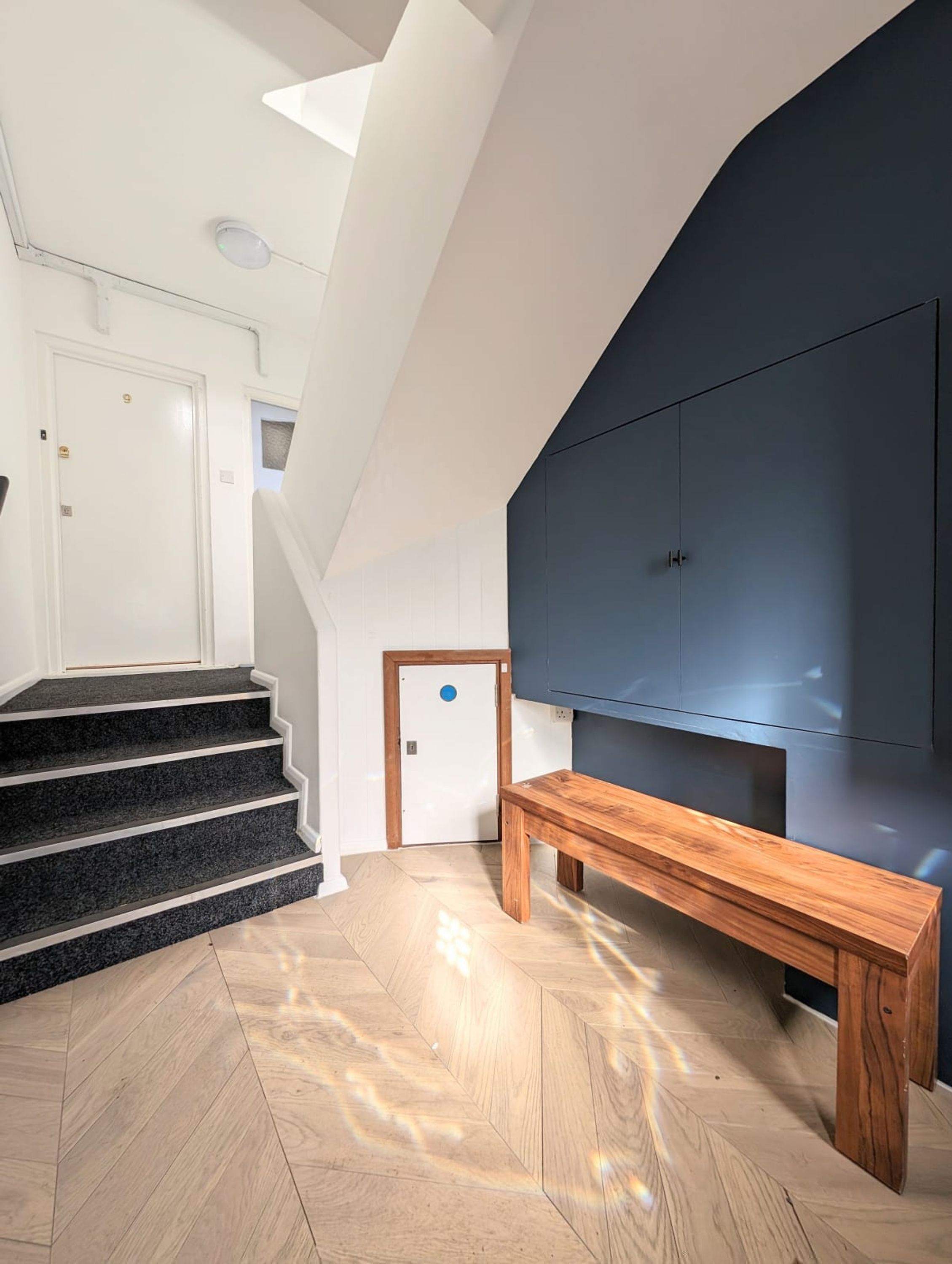 A modern interior with a staircase, a bench, and a dark wall-mounted TV.