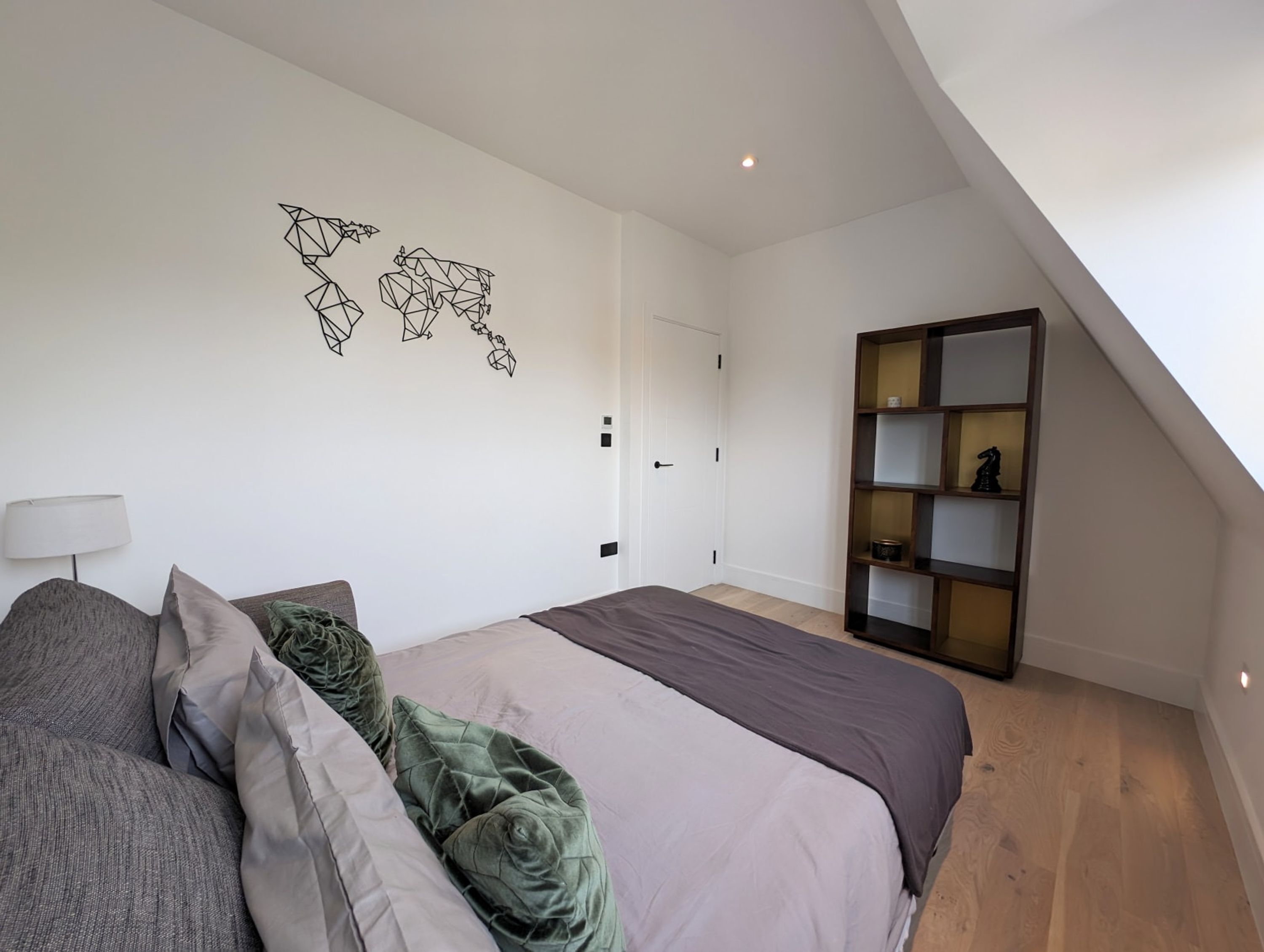 A bedroom with a bed, pillows, a map wall art, a bookshelf, and a door.