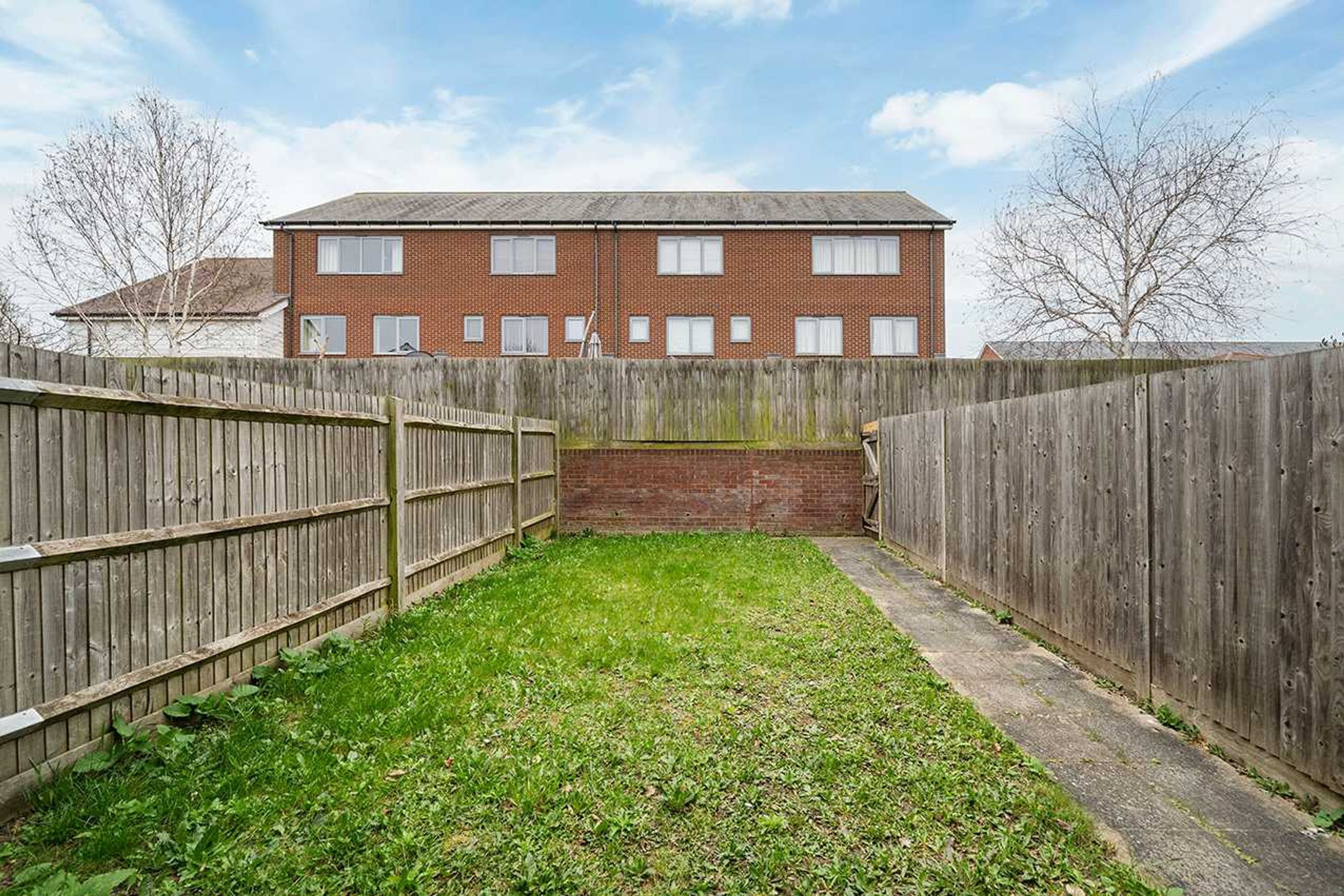 A fenced backyard with a grassy area and a brick building in the background.