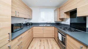 A modern kitchen with wooden cabinets, a gas stove, and a built-in oven. - Charming 2-bedroom House in Northfleet (Gravesend)