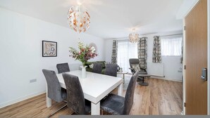 A modern dining area with a white table and grey chairs, a vase with flowers, and a unique spherical light fixture. - Charming 2-bedroom House in Northfleet (Gravesend)