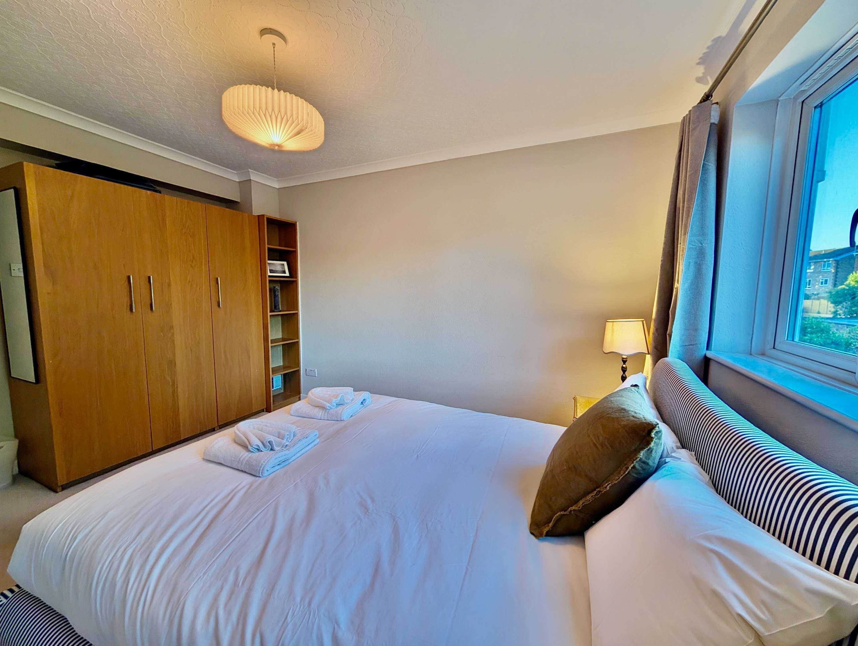 Een hotelkamer met een groot bed, een kledingkast, een nachtkastje met lamp, en een raam met uitzicht.