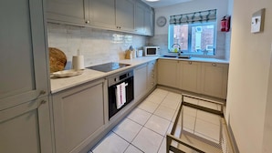 A modern kitchen with grey cabinets, a white countertop, a microwave, and a window with a view of the outside. - Charming Flat Near London Attractions (Surbiton)