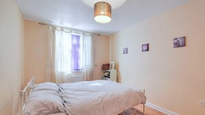 Ein Schlafzimmer mit Bett, einem Fenster mit Vorhängen, einer Deckenleuchte und einem kleinen Teppich.
