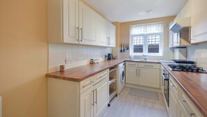 Eine kompakte Küche mit weißen Schränken, einer Holz Arbeitsplatte, einem eingebauten Backofen, einem Geschirrspüler und einem Fenster mit Vorhängen.