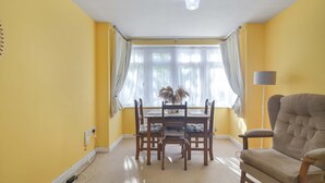 Ein Essbereich mit Tisch, Stühlen, einer Lampe und einem Fenster mit Vorhängen.