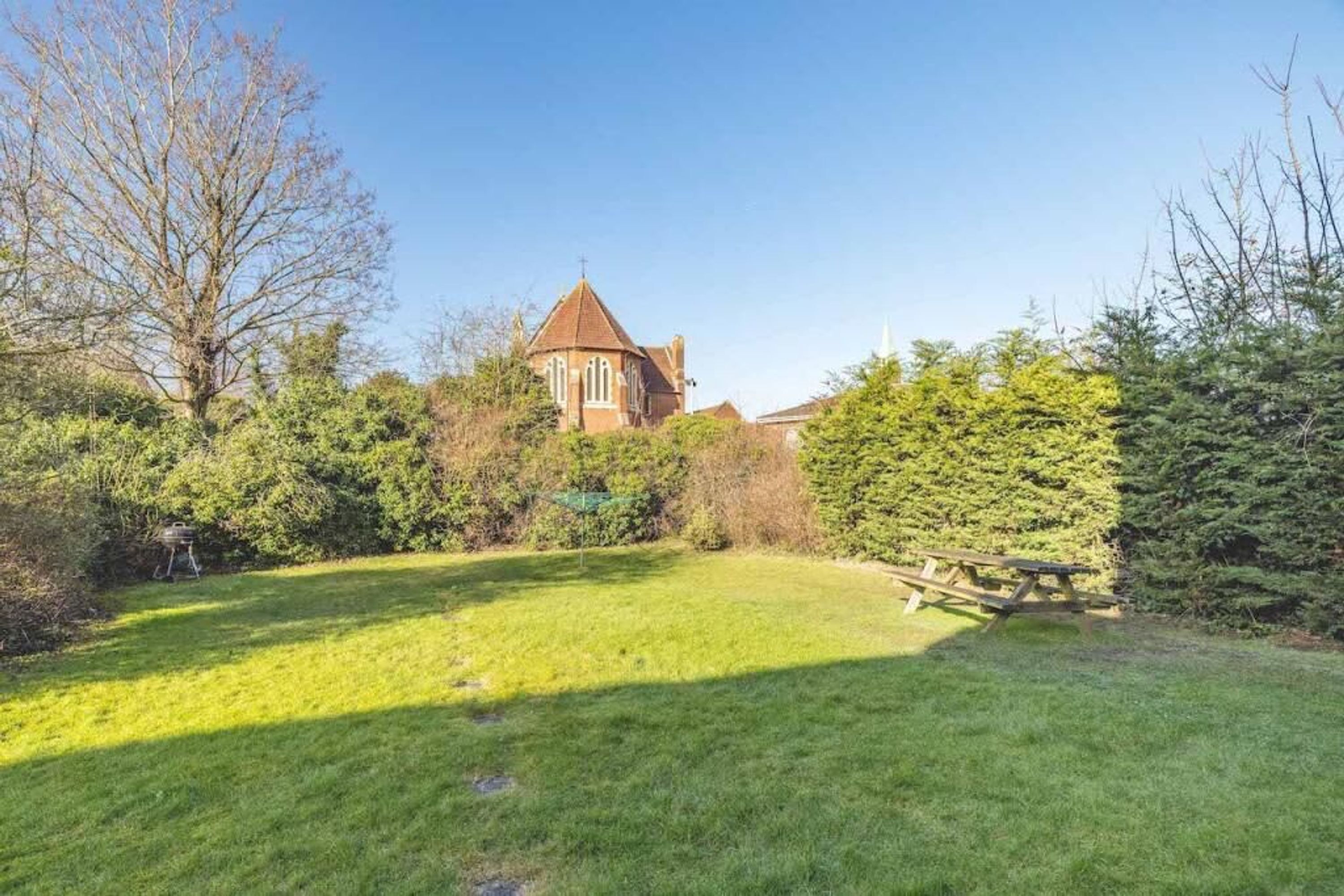 A church with a tower, surrounded by a well-maintained lawn and dense shrubbery.