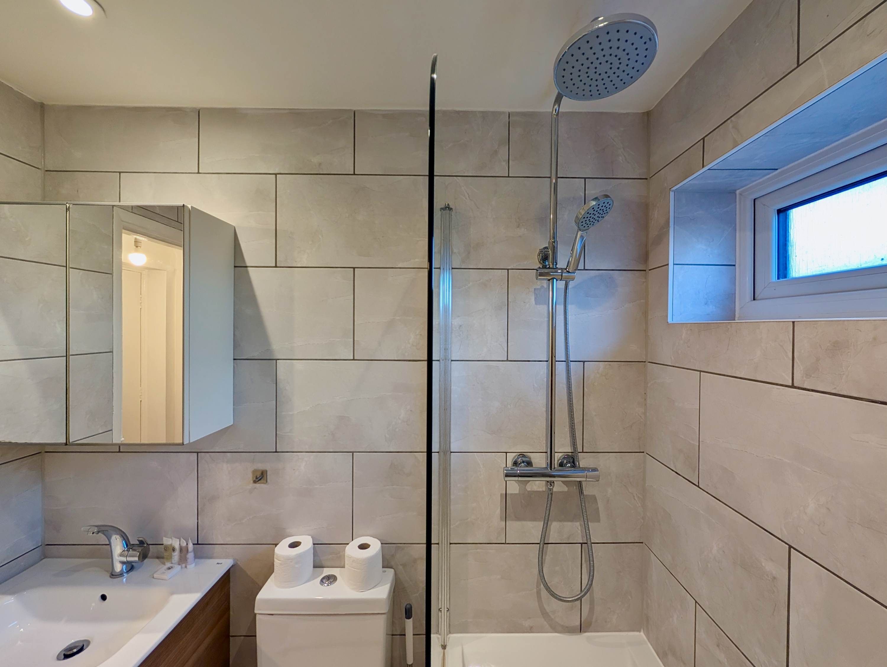 Ein Badezimmer mit Dusche, Toilette, Waschbecken und einem Fenster.