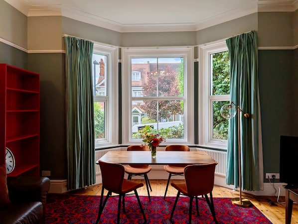 A dining area with a round table, four chairs, a clock, and a red bookshelf. - Charming Two-bedroom House in London (Pinner)