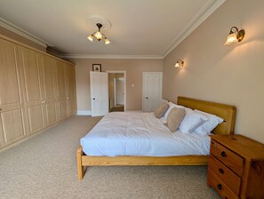 A bedroom with a wooden bed, a wooden nightstand, a wardrobe, and a ceiling light fixture. - Charming Two-bedroom House in London (Pinner)