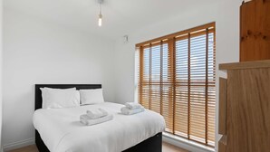 Un dormitorio con cama, ropa de cama blanca, persianas de madera, una lámpara y un armario de madera.