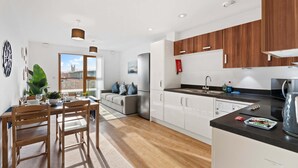 Una cocina moderna con armarios de madera, encimera negra y una zona de comedor con mesa y sillas de madera.
