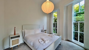 A bedroom with a large bed, bedside tables, a hanging light fixture, and a window with a view of greenery. - Elegant 2-bed Flat in Shenfield (Brentwood)