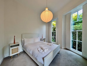 Ein Schlafzimmer mit einem großen Bett, Nachttischen, einer Pendelleuchte und einem Fenster mit Blick auf Grün.