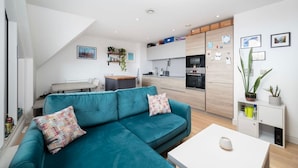 En modern lägenhet med en turkosfärgad soffa, ett vitt soffbord, ett köksområde och ett matbord.