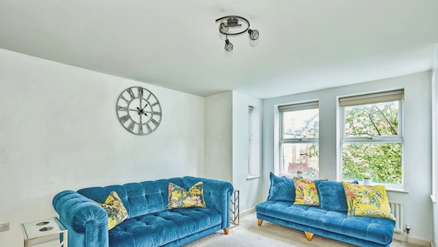 A room with two blue sofas, a wall clock, and a ceiling light fixture.