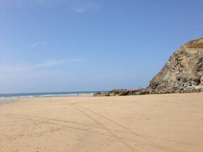 Ein sandiger Strand mit einer felsigen Klippe und dem Meer im Hintergrund.