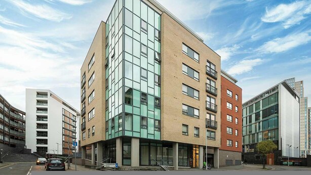 Un immeuble à étages dont les façades sont composées d’un mélange de verre et de briques, et qui est agrémenté de balcons et de grandes fenêtres.