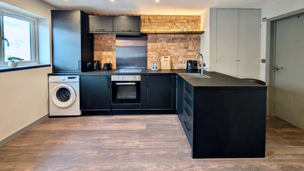 A modern kitchen with a brick backsplash, stainless steel appliances, and a large island. - Charming Flat With Free Parking in Prime Location (Royal Tunbridge Wells)
