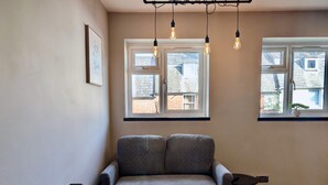 A cozy room with a grey sofa, two windows with views of buildings, and a radiator on the left. - Charming Flat With Free Parking in Prime Location (Royal Tunbridge Wells)