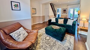 Un salon spacieux avec un fauteuil en cuir marron, un canapé vert et un tapis à motifs.